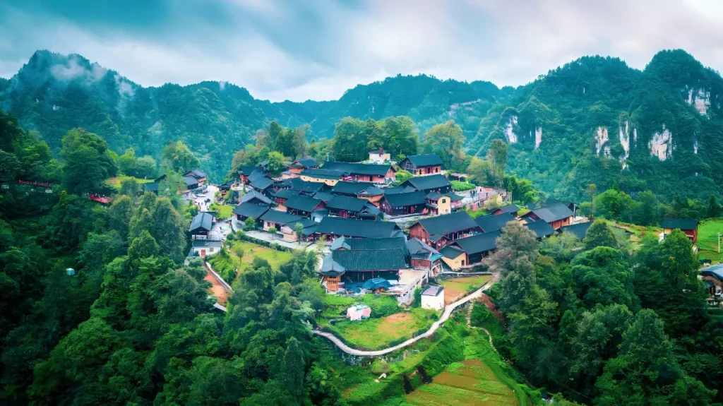 Eighteen Cave Village surrounded by green mountains, forested cliffs and traditional village buildings.