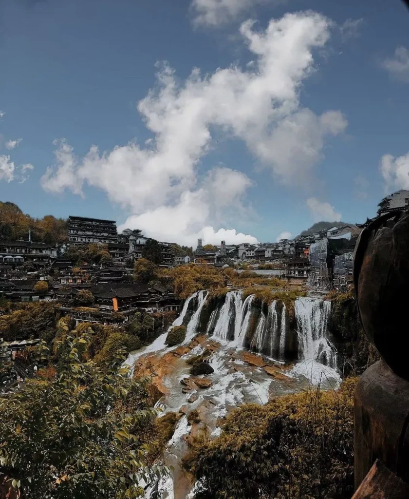 Furong Ancient Town waterfall with cliffside houses and traditional rooftops