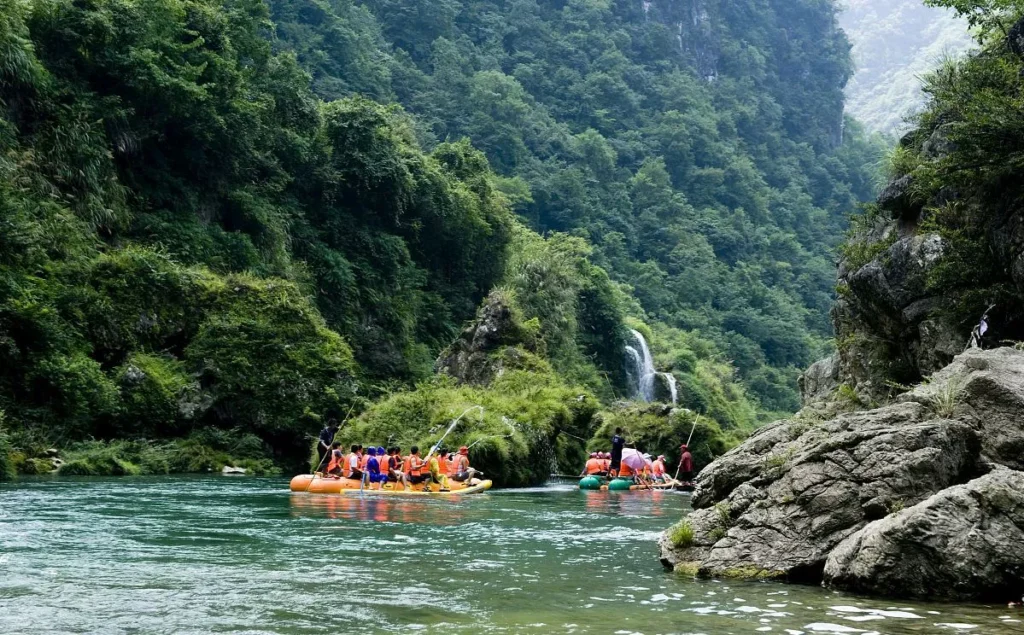 Mengdong River Drifting rafts floating on a clear green river surrounded by forested cliffs and waterfalls.