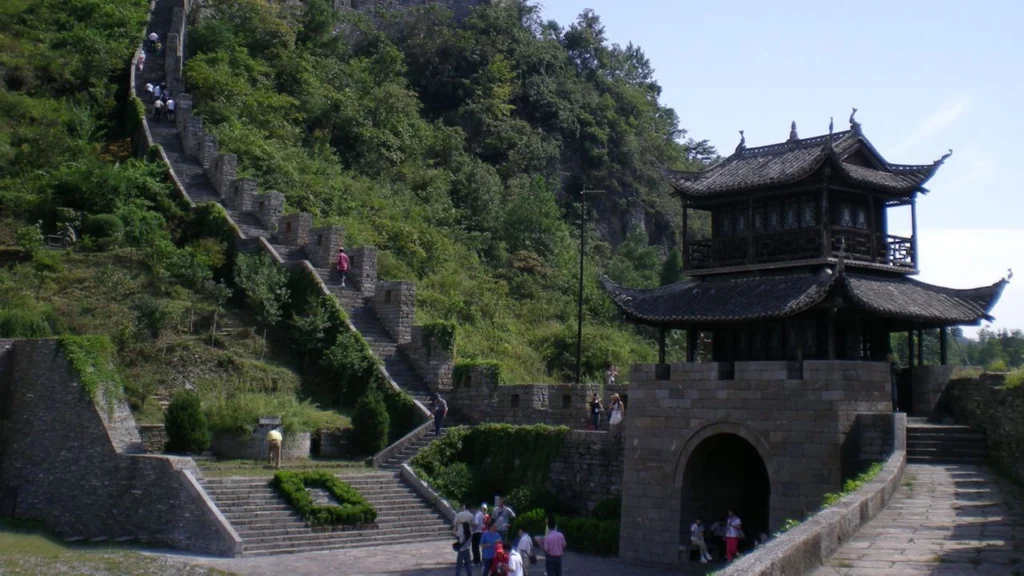 Southern Great Wall gate tower with stone steps, mountain greenery and visitors walking along the wall.