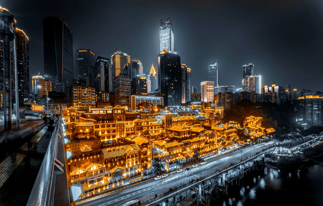 Hongyadong stilted riverside complex glowing gold at night seen from elevated road, Chongqing