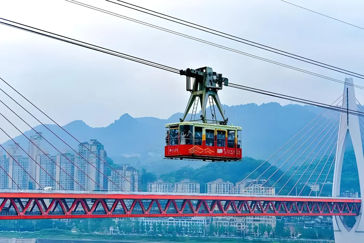 Red Yangtze River Cableway cabin crossing above the river with Dongshuimen Bridge behind, Chongqing