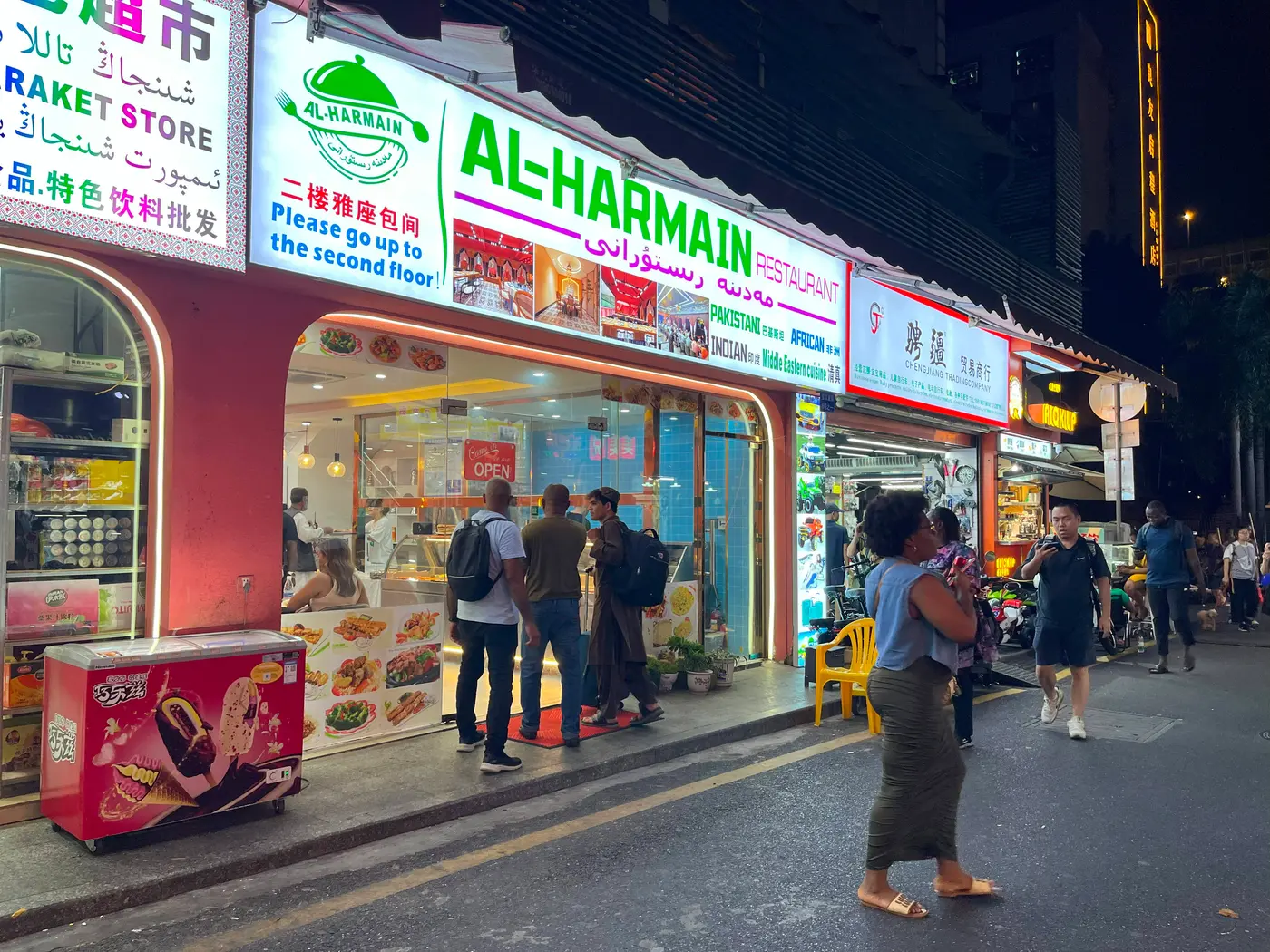 Halal restaurants with Arabic and Uyghur signage on a busy street at night in Guangzhou's Xiaobei Muslim quarter