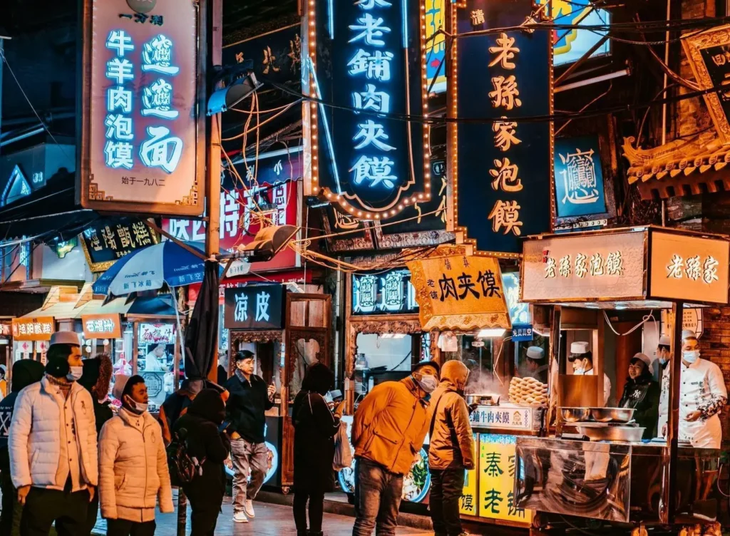 Neon halal food signs and street stalls crowded with visitors at night in the Xi'an Muslim Quarter