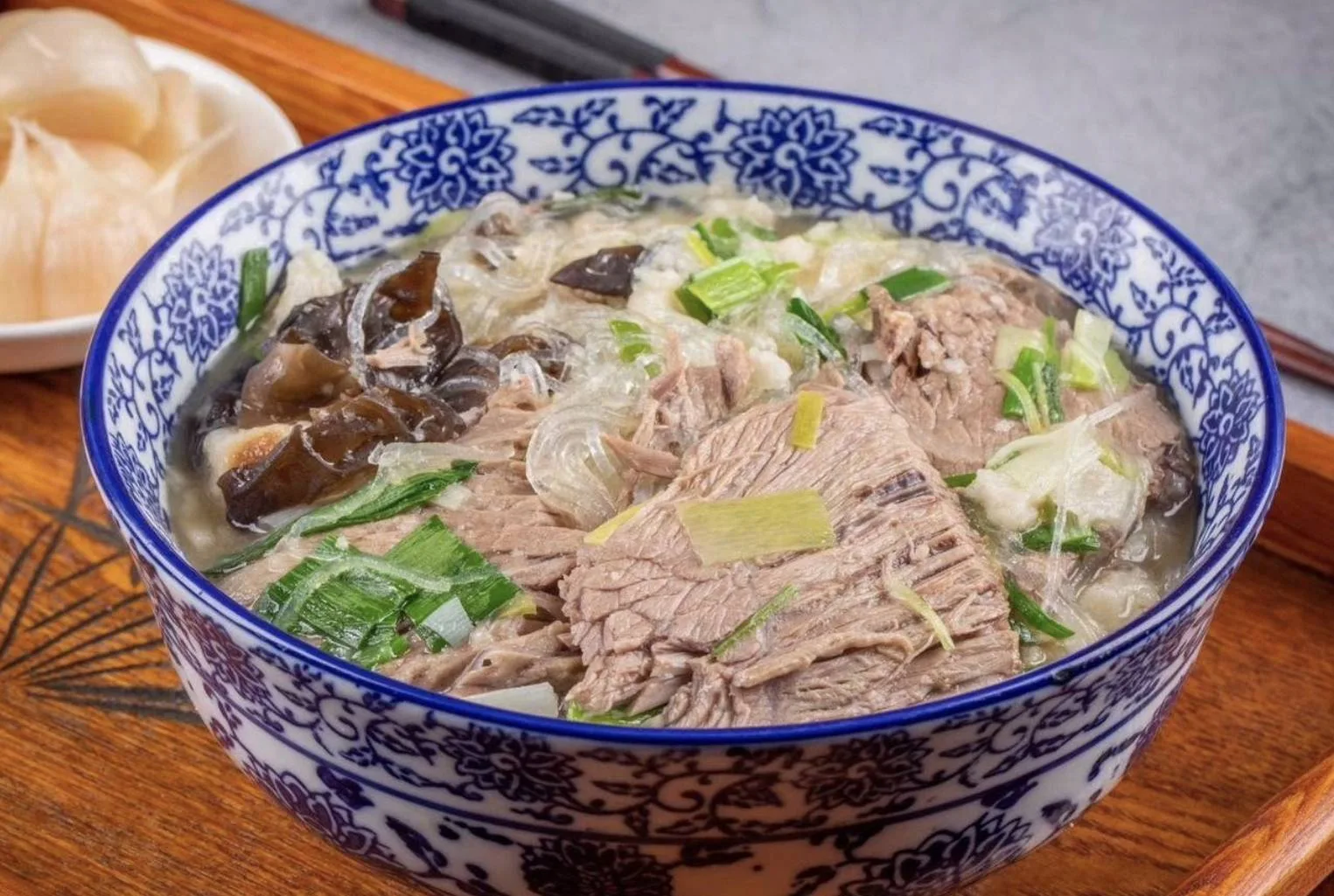 Bowl of paomo with braised beef, glass noodles and crumbled flatbread in broth, with pickled garlic on the side