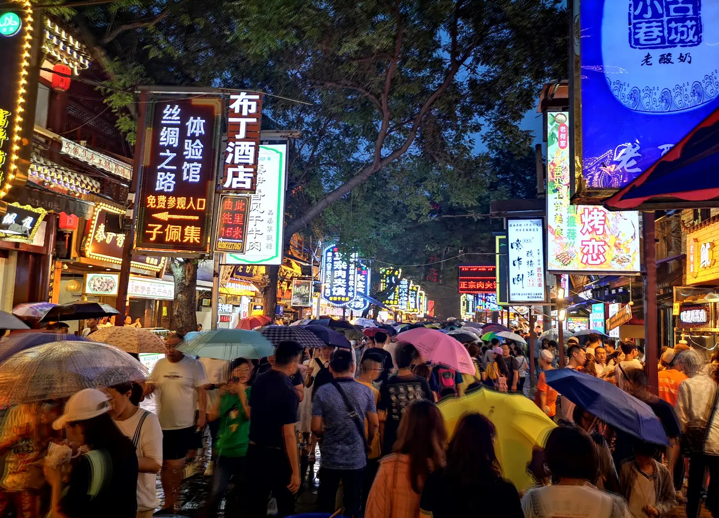 Evening crowds under neon food signs on a street in the Xi'an Muslim Quarter
