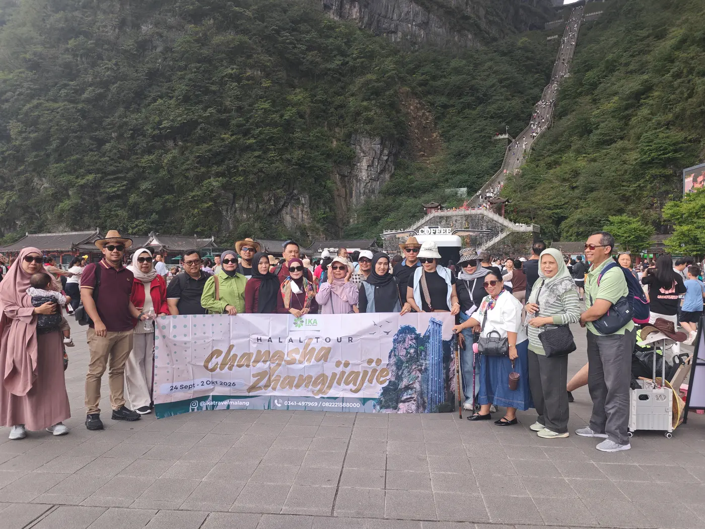 Muslim tour group posing with a halal tour banner at the foot of Tianmen Mountain in Zhangjiajie, with the 999-step stairway behind