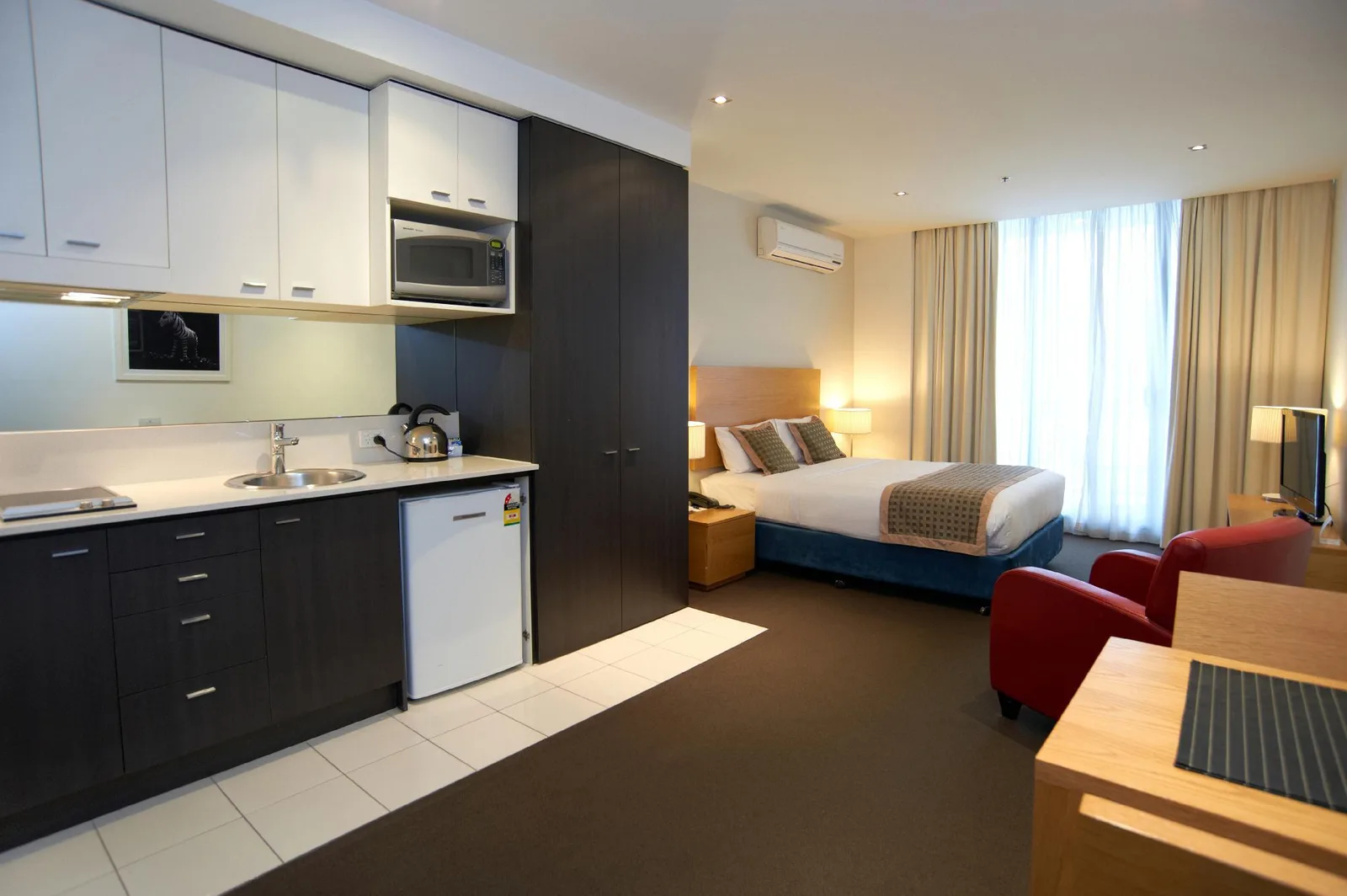 Serviced apartment room in China with a kitchenette including microwave, kettle, fridge and a double bed by the window