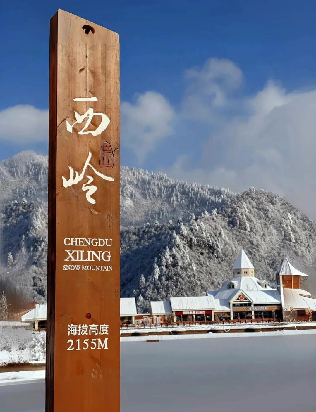 Trailside marker at Chengdu Xiling Snow Mountain showing an altitude of 2,155 m, with snow-covered forest behind